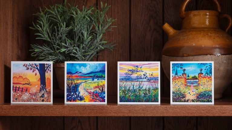 Four brightly coloured illustrated note cards showing autumnal scenes displayed on a shelf
